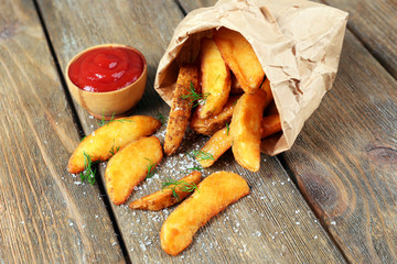 Homemade fried potato in paper bag, on wooden background