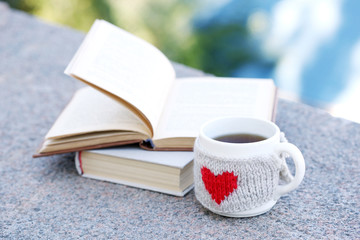 Cup with hot drink and book, outdoors