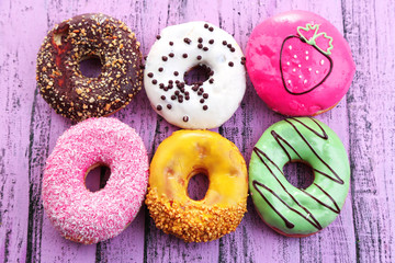 Delicious donuts with glaze on colorful wooden background