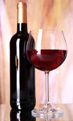 Red wine glass and bottle of wine on bright background