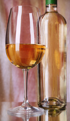 Wine bottle and wineglass with white wine on bright background