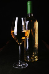 Wine bottle and wineglass with white wine on dark background