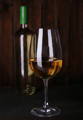 Wine bottle and wineglass with white wine on wooden background