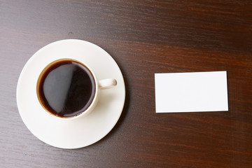 A cup of coffee and a note card on a wooden desk from above