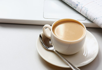 A cup of coffee, paper  on a laptop.