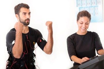 Female coach giving man ems electro muscular stimulation exercis - obrazy, fototapety, plakaty