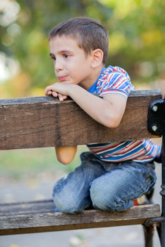 orphan, unhappy boy sitting on a park bench and crying
