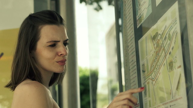 Woman at bus stop looking at map and bus timetable