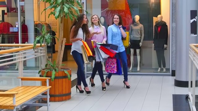 Three beautiful girls with shopping bags goes on shopping center