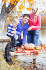 Young family near lake with pumpkins, autumn time