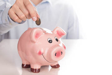 Man's hand putting coin into piggy bank