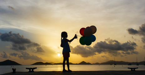 Happy girl with balloons at sunset