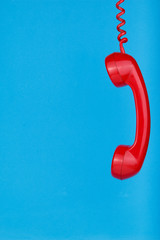 Red telephone hanging on blue background.