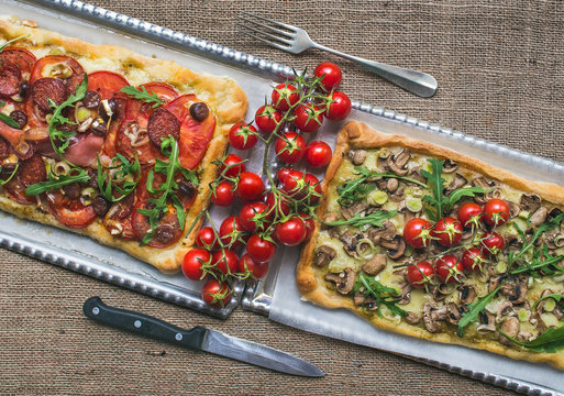 Two square pizzas with fresh arugula and cherry-tomatoes on silv