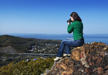 Young woman sitting on the rock and making photo of landscape