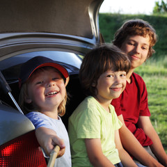 Fototapeta na wymiar Three cheerful child sitting in the trunk of a car on nature