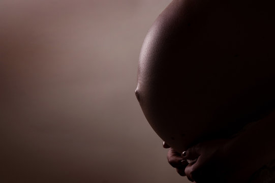 The stomach of the pregnant woman is embraced by hands