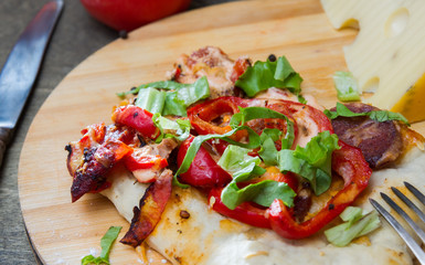 slice of pizza with peppers, bacon and herbs on a wooden board