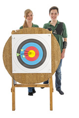 Girl and boy standing behind archery target - 72932659