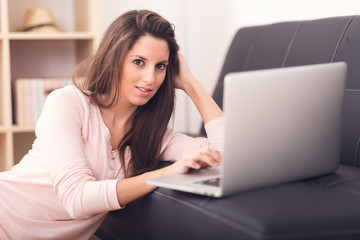 Fototapeta premium Smiling young woman looking on your laptop sitting on floor at h