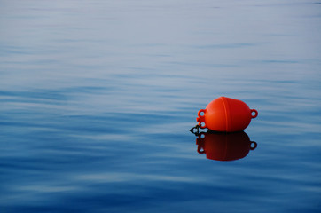 Orange buoy on the tranquil blue water - obrazy, fototapety, plakaty