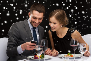 smiling couple with smartphone at restaurant