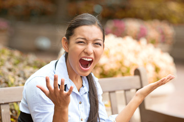 stressed frustrated young woman screaming sitting on a bench 