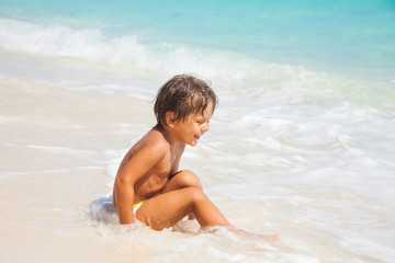 Happy boy sits on the sand beach with white waves