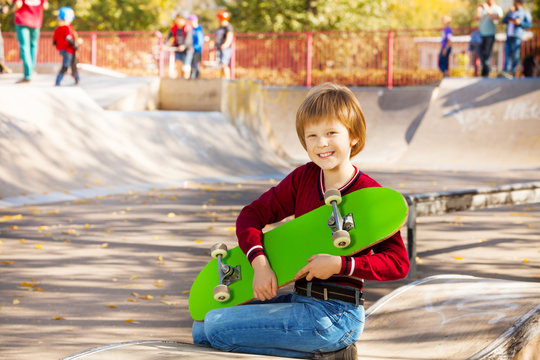 Happy blond boy with green skateboard sitting