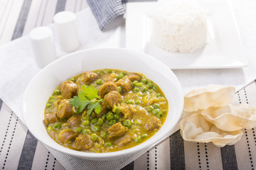 Large bowl of curried sausages with peas and a side of rice and papadum for gluten free meal