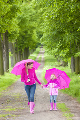 mother and her daughter with umbrellas in spring alley