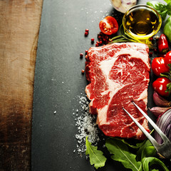 Raw beef steak with meat fork on a dark slate background