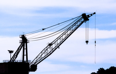 Industrial construction cranes and building silhouettes over sun