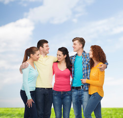 group of smiling teenagers over blue sky and grass