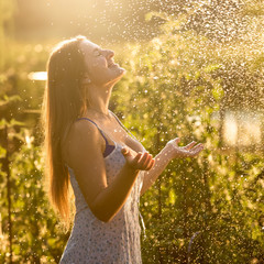 beautiful woman enjoying rain at sunny day at garden