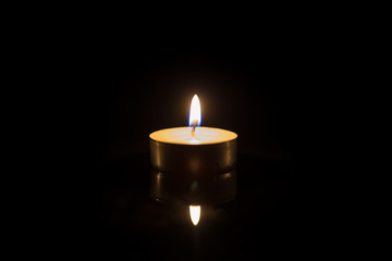 One tea candle with reflection on black