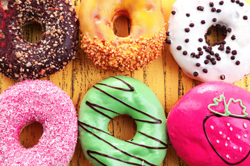 Delicious donuts with glaze on colorful wooden background