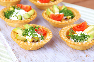 Tartlets with greens and vegetables with sauce on tray on table
