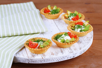 Tartlets with greens and vegetables with sauce on tray on table