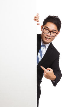 Asian businessman peeking from behind blank banner and point