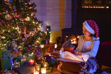 Obraz na płótnie Canvas Christmastime, a young girl in pajamas enjoying to find a teddy
