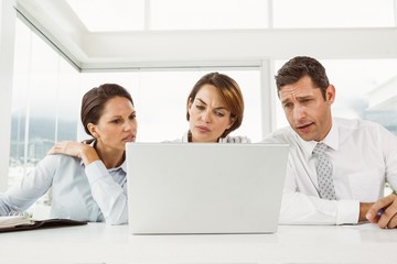 Fototapeta premium Three young business people using laptop at office desk