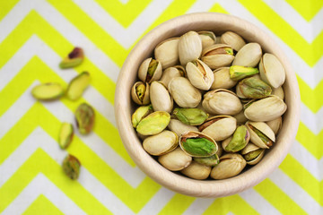 Pistachio nuts in wooden bowl on yellow and white cloth