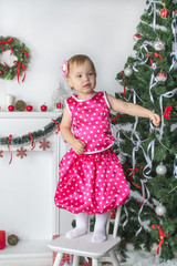 Cute little girl standing on a chair near  the Christmas tree