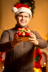 Obraz na płótnie Canvas smiling handsome man in santa hat holding red gift box