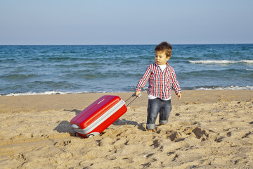 Niño pequeño arrastrando maleta por la arena de la playa
