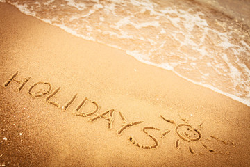 Fototapeta na wymiar The word holidays written in the sand on a beach