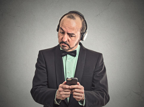 Confused man listening music with headphones on smartphone