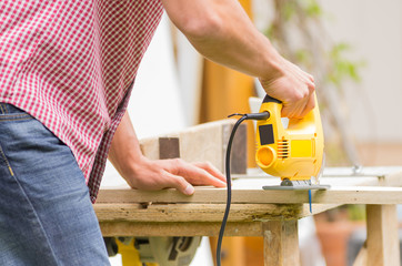 young man carpenter working with electric jigsaw and wood