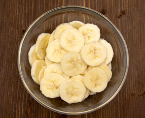 Banana slices on bowl on wooden table seen from above